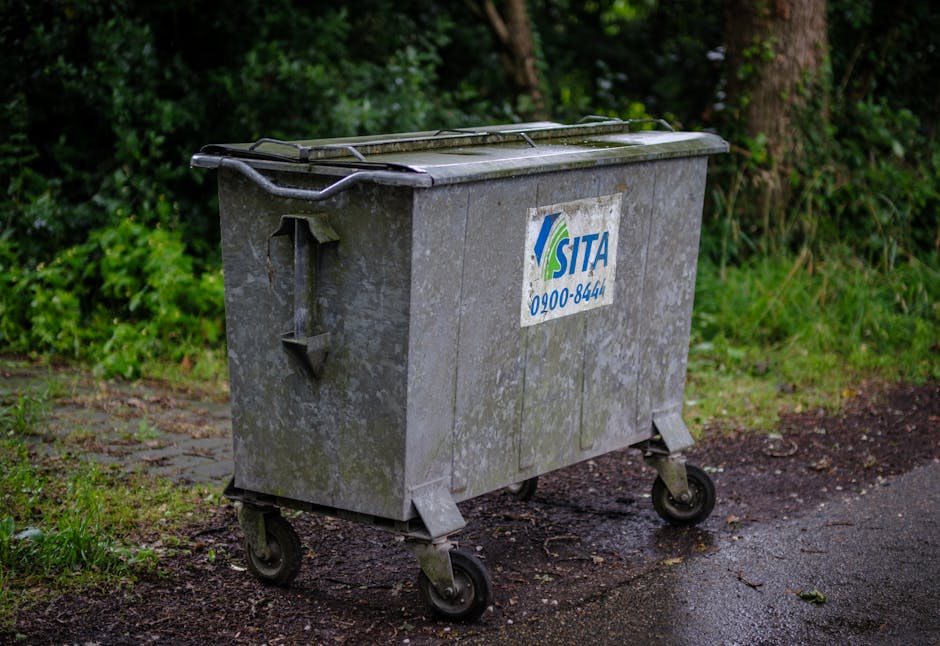 A row of five large commercial waste bins positioned on a paved surface, with four being white and one dark grey, each fitted with lids and marked with labels such as 'WASTE ONLY' and 'ELECTRICAL WAST