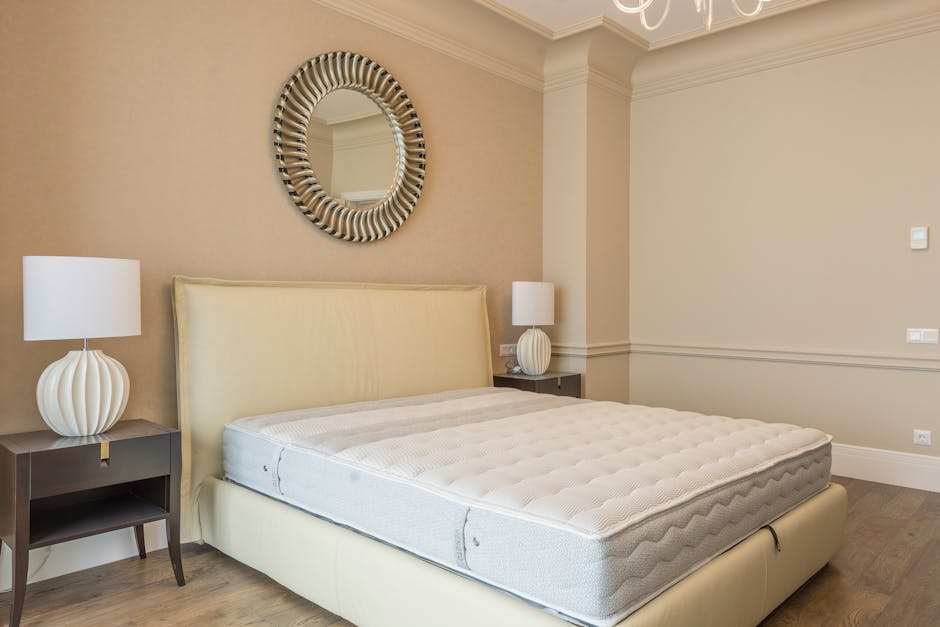 An empty bedroom with white walls and a light wooden floor, featuring a double bed frame without a mattress positioned against the right wall, flanked by small matching bedside tables with black metal